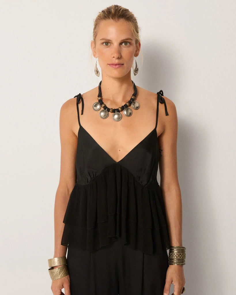 Woman wearing a black sleeveless top with ruffled details against a plain background