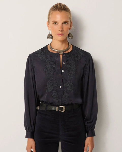 Woman wearing a dark blouse with lace details against a plain background
