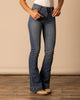 Person wearing blue jeans and a white top on a wooden floor with a beige wall background